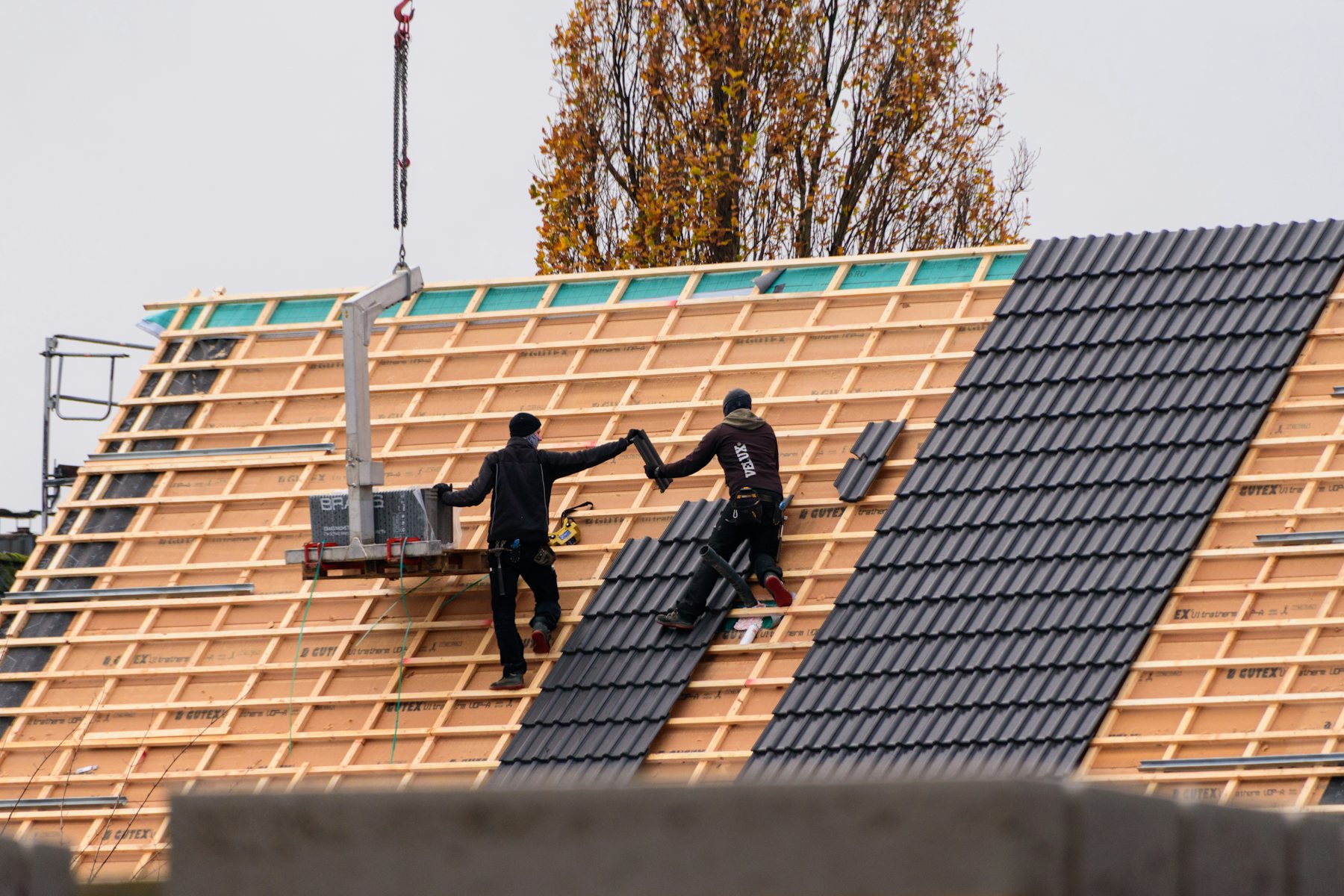 Two roofers laying dark grey interlocking roof tiles over new timber battens