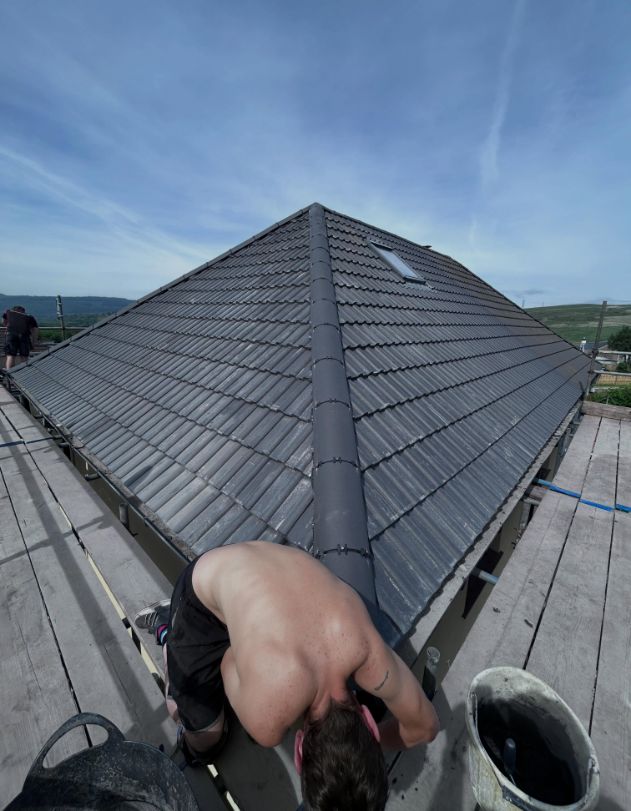 Concrete tile hip roof under construction with roofer at work